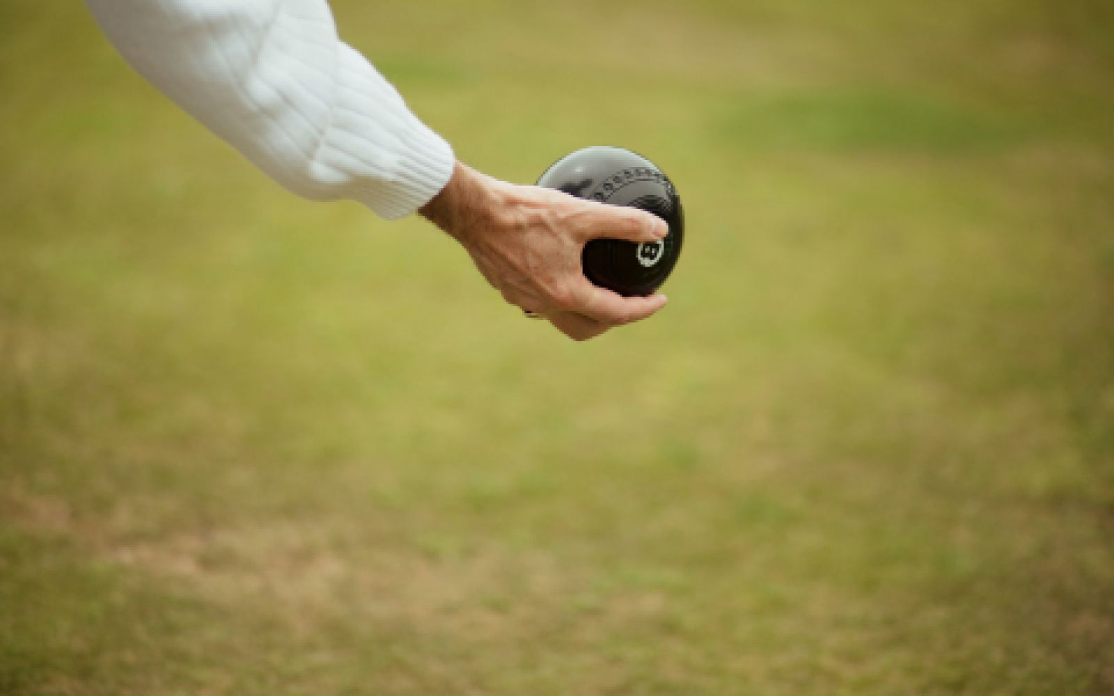 Parksville Lawn Bowl Club member's hand lawn bowling with green grass in the background