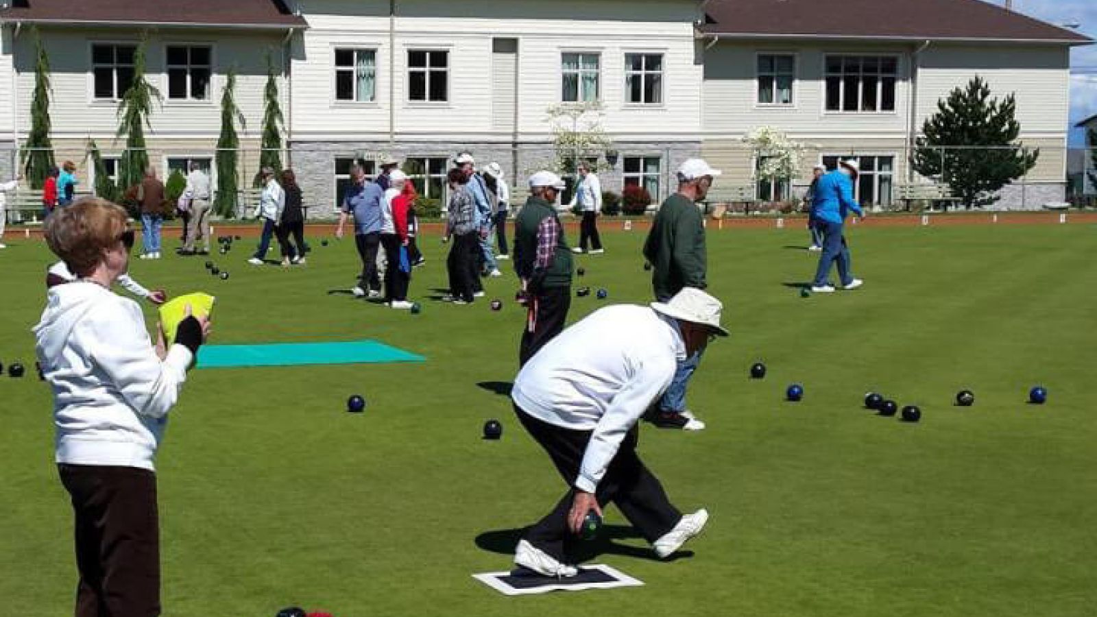 Parksville Lawn Bowling Club members lawn bowling with building and blue skies in the background